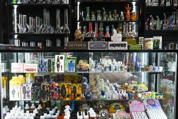 Wall display of glass water pipes and bongs above a glass case of accessories